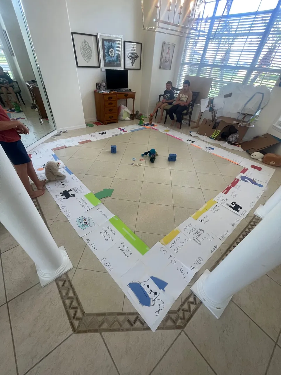 Children beside a giant handmade board game drawn on paper and laid out across a floor.
