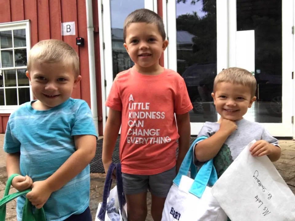 Three young brothers sitting together outdoors with their arms around each other.