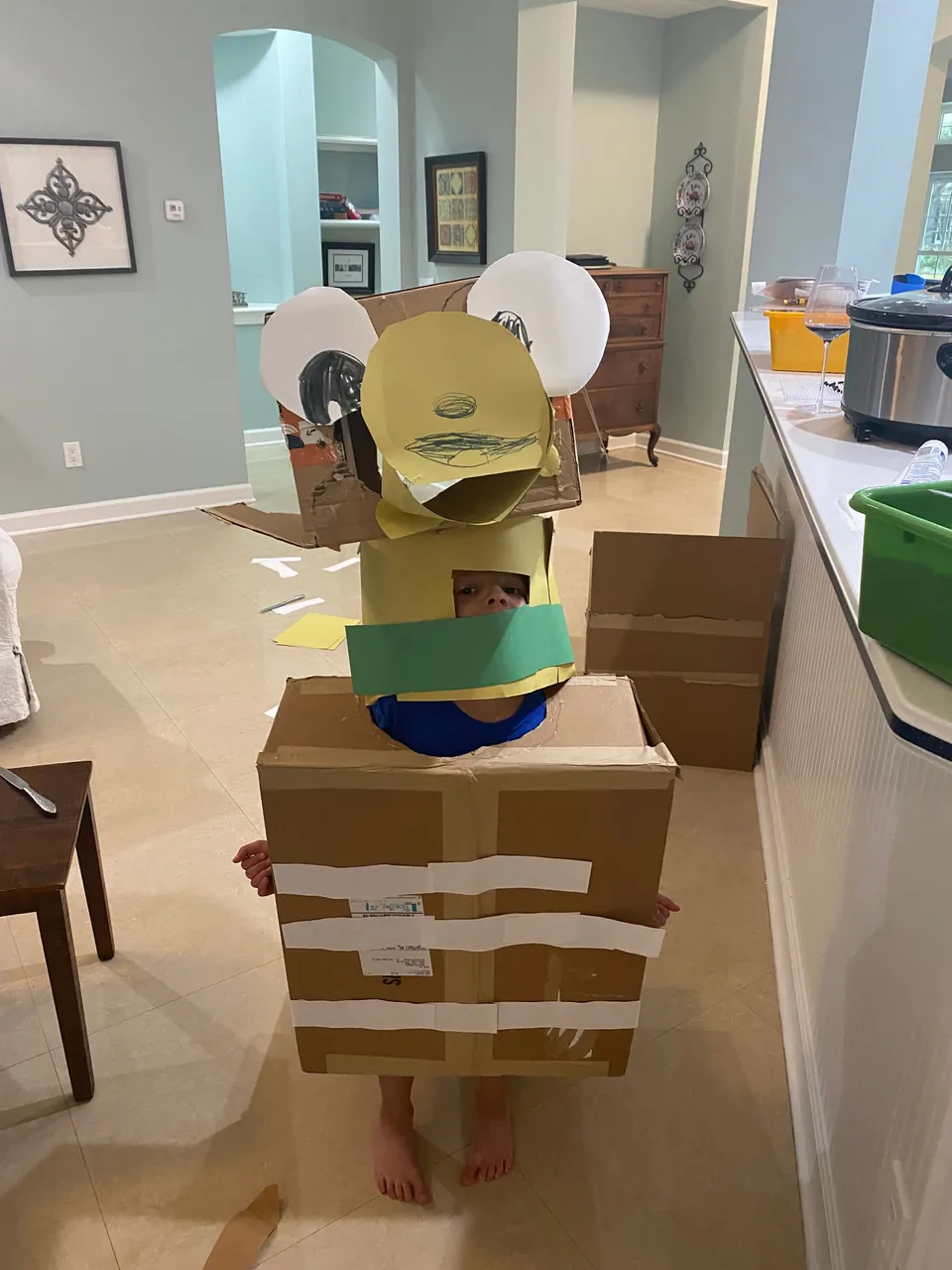 Child wearing a large handmade cardboard and paper character costume built from shipping boxes.